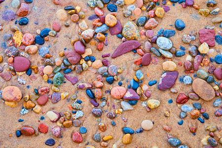 闪亮的红色、黑色、蓝色、粉色和紫色多色石头映衬在沙滩上