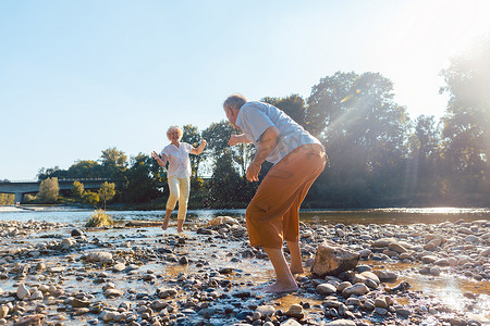 风趣的老年夫妇在阳光明媚的日子里在河边玩水