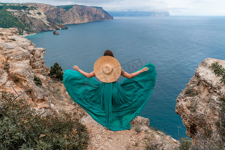 一件绿色礼服的一个美丽的女孩跑向海，以大岩石和海为背景