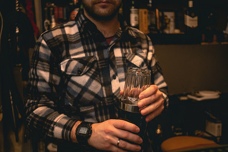 制酒摄影照片_酒保拿着摇酒器和玻璃杯，混合鸡尾酒的配料
