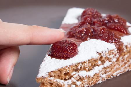 草莓巧克力塔摄影照片_手拿着一块蛋糕，上面有草莓酱和糖。