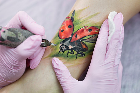 专业纹身师在一个年轻女孩的腿上纹身。