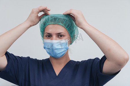 灰色背景下戴着医用口罩和手术帽的女医生或科学家的特写。
