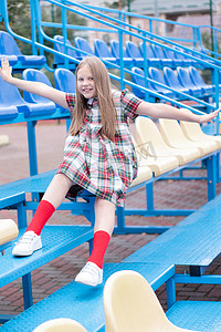 蓝色校服摄影照片_学校体育场蓝黄相间的看台上穿着校服的漂亮女孩。