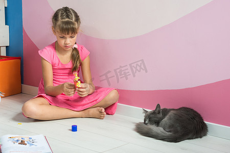一个女孩正在用彩纸制作人物，一只家猫正在附近睡觉