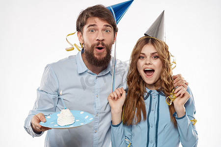 精力充沛的男女带着蛋糕和帽子在浅色背景下庆祝生日
