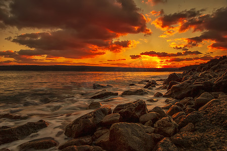长时间曝光日落在海面上晒太阳，沙滩上有岩石。