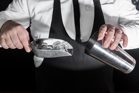 专业酒保的手将冰块放入一个用于准备和混合酒精鸡尾酒的工具，一个金属摇壶
