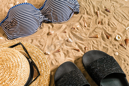 夏季比基尼和配饰时尚沙滩套装、沙滩比基尼夏季服装和海沙为背景、顶视图、概念