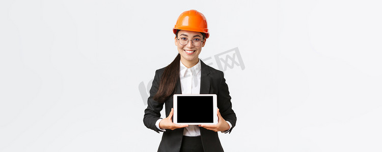 微笑的亚洲专业女建筑师介绍她的项目，工程师在数字平板电脑显示器上展示图表，在企业或工厂进行演示，站在白色背景