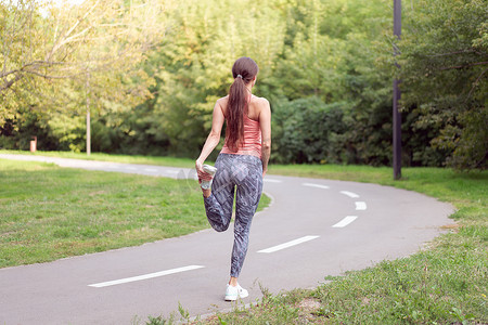 在夏日公园的跑道上，适合女性在跑步前热身腿
