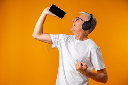 老人戴着耳机听音乐，手持智能手机如麦克风