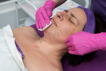 眼睛闭摄影照片_在整容过程中，美容师用化妆垫擦拭脸上的皮肤