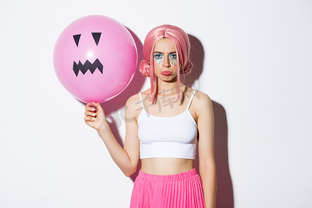一张阴郁失望的派对女孩的照片，她化着鲜艳的妆容，戴着粉色假发，拿着杰克灯笼脸的气球，庆祝万圣节
