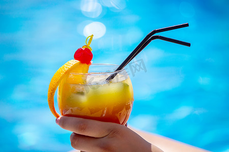 榨摄影照片_泳池边躺椅上的一个女孩喝着鲜榨橙子鸡尾酒。