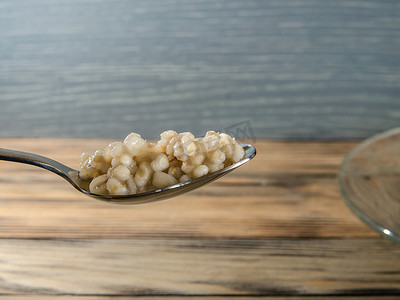 珍珠粉摄影照片_木质背景中勺子中的热珍珠大麦粥