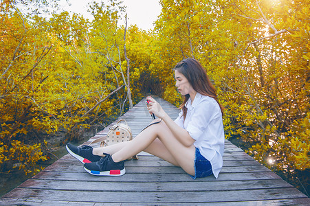 秋天，女孩独自坐在木桥上，手拿相机。