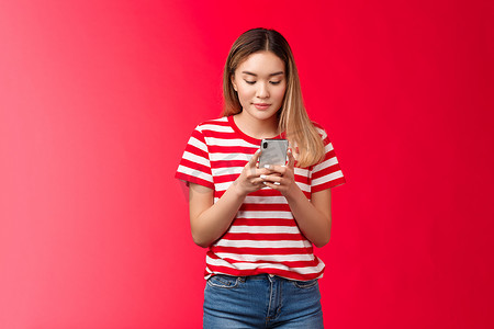 流行的亚洲女性生活方式博主在网上发布照片，拿着智能手机看手机显示滚动提要，女人微笑着高兴地放松，使用小工具站红色背景