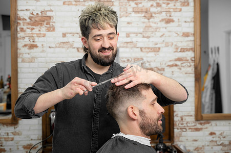 剪头发摄影照片_理发师用剪刀给一个英俊的小伙子剪头发。