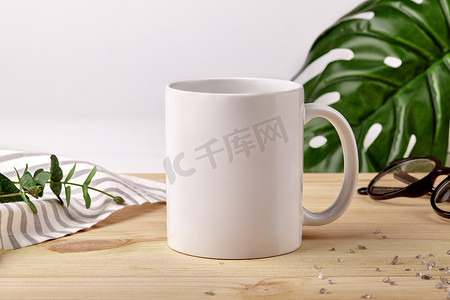 木制桌面上的陶瓷杯，旁边是条纹桌布、散落的水晶和白色背景的绿色植物。