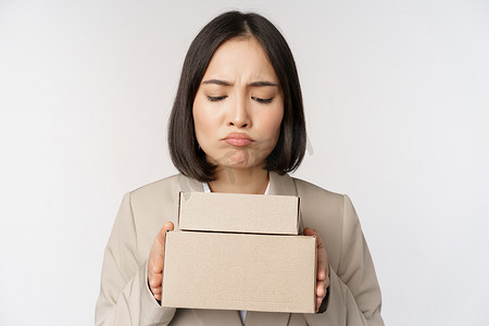 女脸手摄影照片_亚洲女售货员、女企业家拿着盒子，站在白色背景下看起来悲伤、失望的画像