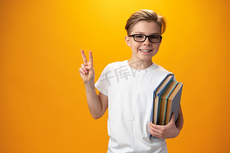 黄色背景下拿着一本书的小男学生