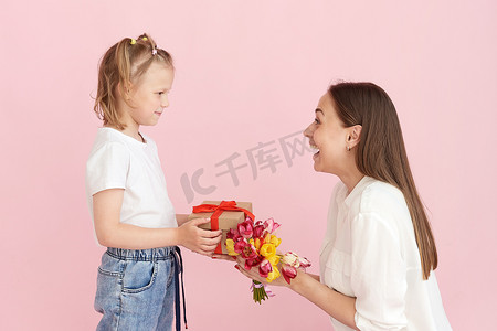 在工作室里，一个小女儿在粉色背景下给妈妈送花和母亲节礼物。