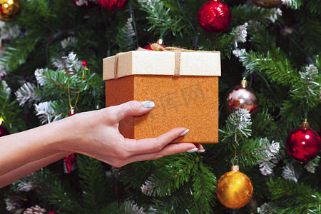 女手拿着礼盒，顶着装饰精美的圣诞树