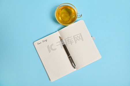 平躺的开放式记事本，上面写着“亲爱的日记”，蓝色背景的茶杯旁边有一支墨水笔，有复制空间