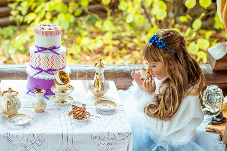 爱丽丝梦游仙境风景中一个小漂亮女孩在公园的桌子上喝茶的侧视图