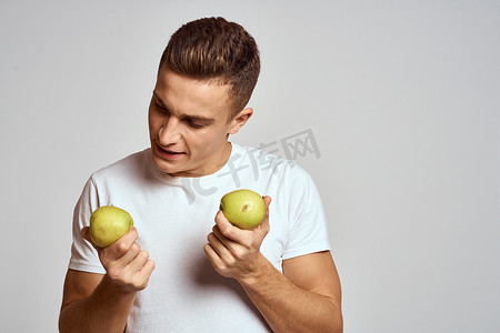 一个手拿苹果的男人，背景浅，身穿白色 T 恤，双手微笑着指手画脚