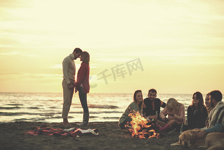 一对夫妇在日落时分在海滩上与朋友一起享受