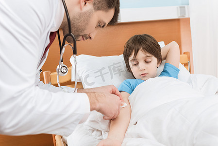 床上的男孩摄影照片_身穿医用制服的医生给床上的男孩病人注射