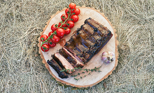 传统欧洲风格的烧烤排骨肉，配以迷迭香香草樱桃番茄和大蒜，在干草背景的生实木切割板上