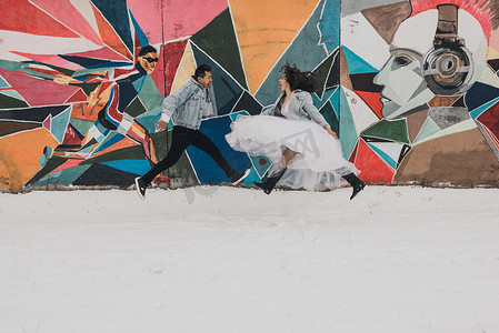 Khmelnytskyi，乌克兰 — 27.11.2018：冬天穿着婚纱和牛仔夹克的新婚夫妇在流行艺术街上跳来跳去