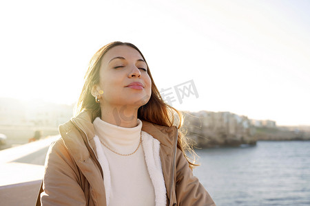 呼吸新鲜空气摄影照片_年轻迷人女性的肖像，呼吸新鲜空气，闭着眼睛在沙滩上放松