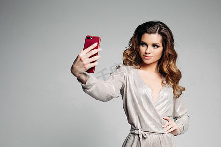 身穿银色连衣裙的 Sudactive 女模特在智能手机上拍照。