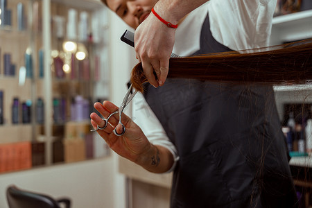 剪头发摄影照片_美发师手拿着梳子的特写，同时为女性剪头发