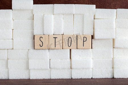 过量摄影照片_堆或墙的糖块和大写字母的停止词，作为对成瘾卡路里过量和甜味不健康食物滥用导致健康问题和超重背景的建议