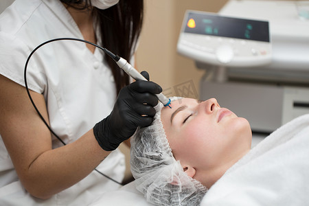 治疗师美容师在美容水疗诊所对年轻女性的脸部进行激光治疗。