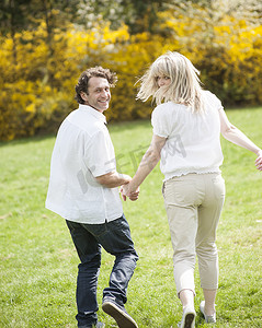 情侣牵着手摄影照片_一对情侣牵着手背对着镜头穿过公园