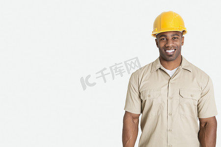 灰色背景中戴着黄色安全帽头盔的快乐非洲年轻男子的肖像
