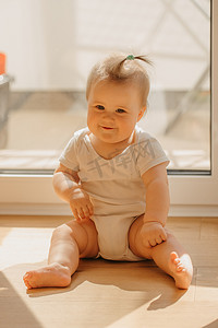 一个善良的 7 个月大女孩正坐在家里的阳台门附近，穿着紧身连衣裤
