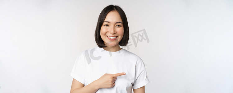 快乐美丽的亚洲女孩在空白的复制空间上展示广告，手指向右，微笑，展示横幅或公司标志，白色背景