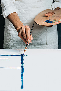 一位老妇人用蓝色颜料在画布上绘画的工作室图像。