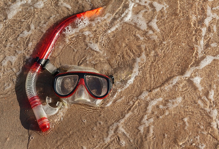 面罩和通气管躺在潮湿的沙子上，波涛汹涌
