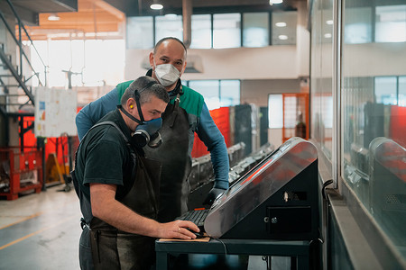 两名因冠状病毒大流行而戴着口罩的工人正在为一台现代数控机床编程