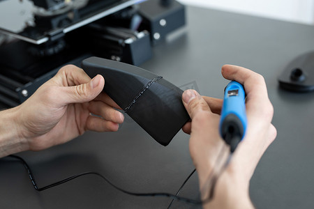 男子用 3D 笔连接两个 3D 打印机部件。