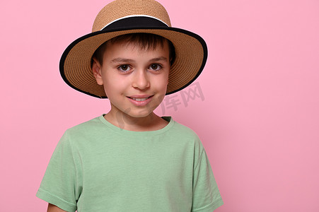 一个戴着夏日草帽的帅气男学生的特写，他看着相机，站在粉色背景中，与世隔绝，有复制空间