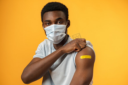 接种疫苗的非洲裔美国人在黄色背景下展示他的手臂